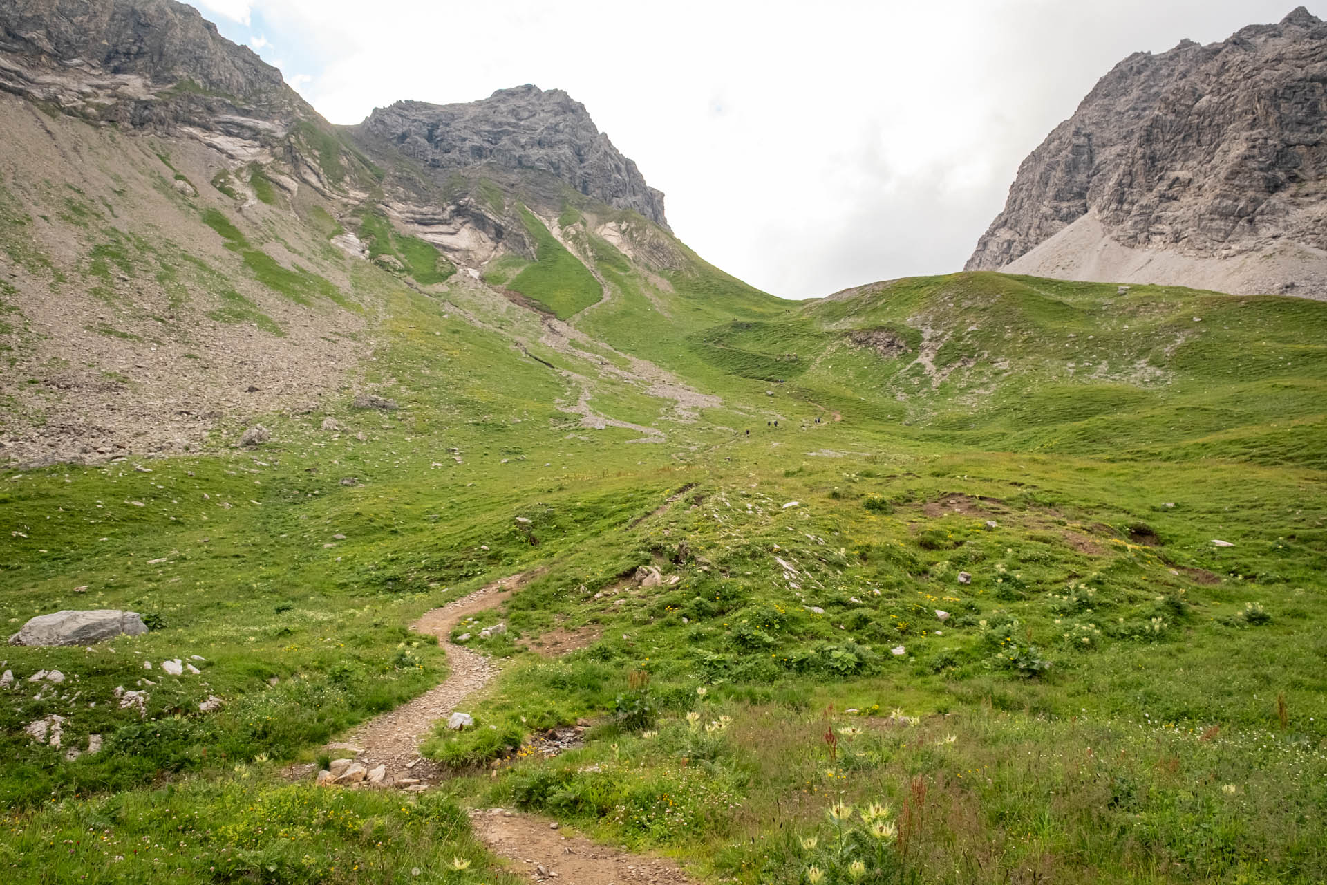 Aufstieg über Gras und Fels mit Bergen im Hintergrund